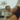 A close-up outdoor portrait features a joyful African American mother holding her baby son. Both are smiling widely with eyes closed, expressing genuine laughter and happiness, their faces beautifully lit by golden hour sunlight which backlights the mother's curly hair. In the soft background, a suburban house and greenery are visible, emphasizing the warm, loving interaction.
