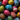 A vertical, overhead photograph showcasing dozens of vibrantly colored Easter eggs, densely packed to completely fill the frame. Each egg is uniquely hand-decorated with intricate patterns like dots, swirls, stripes, and floral motifs in bright hues of red, blue, yellow, pink, green, and white, set against a dark background, highlighting their artistic detail and festive appeal.
