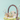 A charming brown wicker basket is centered against a soft light blue background, filled with two miniature pastel-colored houses. Artificial green grass and several speckled Easter eggs in soft hues of blue, green, and pink are nestled around the houses within the basket. Pussy willow branches emerge from behind the houses, and additional pastel Easter eggs are scattered around the base of the basket on the matching light blue surface, creating a whimsical spring holiday scene.