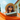 A low-angle shot of a young woman smiling and relaxing in a bright orange hammock under a clear blue sky. She wears a straw hat and dark sunglasses, holding a book, with a blurred background showing green trees and a large, light peach-colored building with white columns and a red roofline.