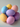 A close-up shot of a small pile of decorative speckled eggs in various pastel colors, including light yellow, pale blue, lavender, and soft pink. The eggs are stacked loosely against a minimalist, light gray background, with soft lighting highlighting their gentle textures and shades.
