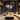 A luxurious modern living room at night, featuring a cream L-shaped sofa and a marble coffee table laden with wine, golden champagne flutes, and a bottle of champagne in a gold bucket. Through expansive floor-to-ceiling windows, a vibrant display of golden fireworks illuminates a sprawling city skyline, evoking a sense of festive opulence and high-rise celebration.