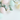 A top-down flat lay shot showcases five pastel-colored Easter eggs scattered across a bright white background, interspersed with fresh eucalyptus branches and tiny white flowers. The eggs are primarily pale pink, mint green, and light yellow, creating a soft, inviting color palette. The composition leaves substantial white space in the lower half of the vertical image, allowing for easy text or graphic overlays.