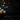 A low-key image shows a brown woven basket positioned on the left, filled with several brightly colored, patterned Easter eggs in shades of blue, yellow, orange, and pink. The background is dark and blurred, illuminated by numerous warm golden bokeh lights scattered softly around the basket.