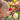 A close-up, side profile of a baby with light hair and fair skin is captured looking intently at a cream-colored tulip in the foreground. The baby's right hand, with small fingers, is slightly extended towards the flower as if to touch it. The background features a vibrant, out-of-focus garden filled with numerous colorful tulips in shades of red, pink, yellow, and purple, all bathed in soft, warm natural light, suggesting a beautiful spring day.