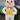 A full-body image of a white Easter bunny mascot standing upright. The bunny has large white ears with pink insides, an orange nose, black eyes, and pink blushed cheeks, wearing a vibrant yellow vest with colorful, dandelion-like patterns, purple buttons, and a purple bow tie featuring small illustrations. It sports bright fuchsia shoes with similar patterns and is positioned outdoors against a background of a large blue flower mural and green foliage, standing on a dark paved surface.