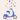 A whimsical digital illustration depicts a white cartoon rabbit with long ears, wearing a white long-sleeved shirt and blue pants, riding a bright blue vintage-style scooter. The rabbit holds a patterned orange Easter egg in its hands and looks upwards at a cascade of colorful, elaborately decorated Easter eggs floating in the air above it. The background is a plain, light beige color, creating a clean and cheerful composition.